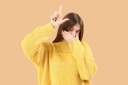 Photo for Laughing young woman showing loser gesture on beige background - Royalty Free Image