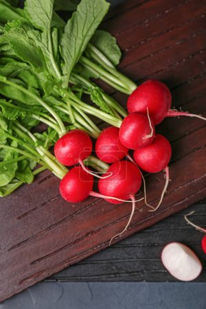 Photo for Wooden board of ripe radish with green leaves on dark background - Royalty Free Image