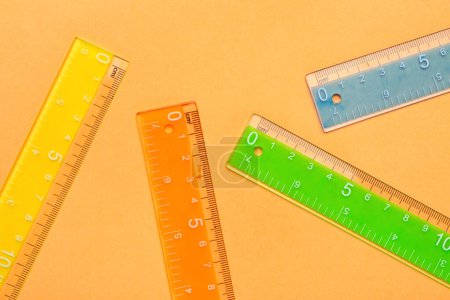 Colorful plastic rulers on orange background
