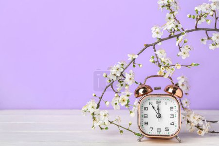 Blooming spring branches and alarm clock on white wooden table near purple wall