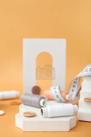 Photo for Podiums with thread spools and buttons on orange background, closeup - Royalty Free Image