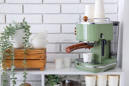 Machine à café moderne avec tasses et plantes d'intérieur sur étagère près du mur de briques blanches