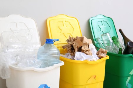 Foto de Papeleras con símbolo de reciclaje y diferentes basura cerca de la pared blanca - Imagen libre de derechos
