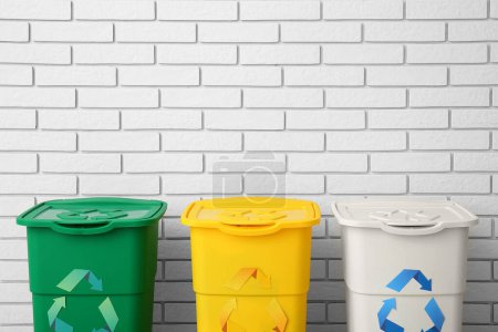 Foto de Diferentes contenedores de basura con símbolo de reciclaje cerca de la pared de ladrillo blanco - Imagen libre de derechos