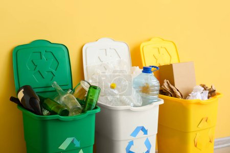 Foto de Papeleras con símbolo de reciclaje y diferentes basura cerca de la pared amarilla - Imagen libre de derechos