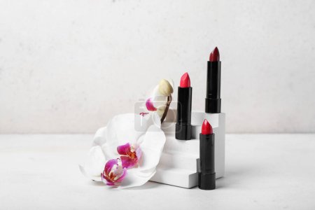 Téléchargez les photos : Podium en plâtre décoratif avec des rouges à lèvres et des fleurs d'orchidée sur table blanche - en image libre de droit