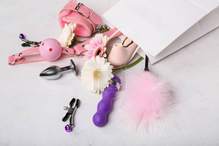 Paper bag with sex toys and flowers on white background, closeup