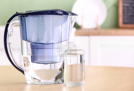 Modern filter jug and glass of water on wooden table in kitchen