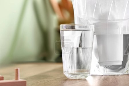 Glass of water near modern filter jug on kitchen counter, closeup