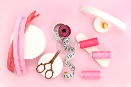Photo for Podiums with scissors, thread spools, measuring tapes and zips on pink background - Royalty Free Image