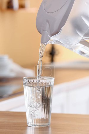 Verter agua de la jarra de filtro moderna en vidrio en el mostrador de la cocina