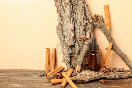 Photo for Bottle of essential oil with cinnamon sticks, anise and tree barks on table near beige wall - Royalty Free Image