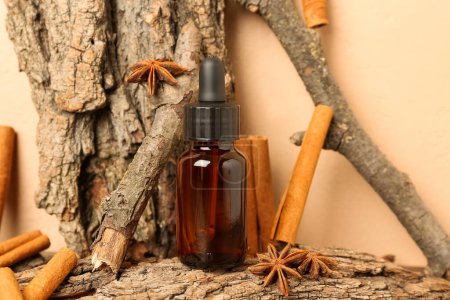 Photo for Bottle of essential oil with cinnamon sticks, anise and tree barks on table near beige wall - Royalty Free Image