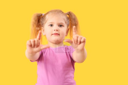 Photo for Funny little girl showing loser gesture on yellow background - Royalty Free Image