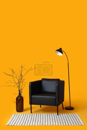 Foto de Moderno sillón negro, lámpara y jarrón con ramas sobre fondo naranja - Imagen libre de derechos