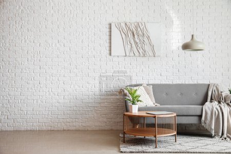 Téléchargez les photos : Canapé gris et table basse avec ordinateur portable moderne près du mur de briques blanches - en image libre de droit