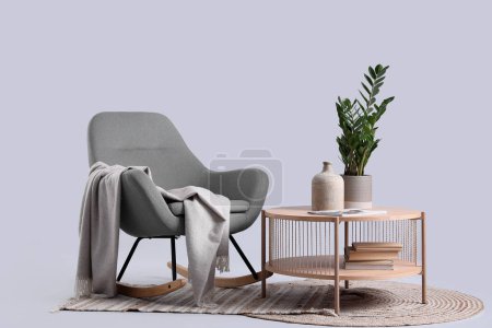 Téléchargez les photos : Table basse en bois avec plante d'intérieur et vase près d'un fauteuil à bascule confortable sur fond gris - en image libre de droit