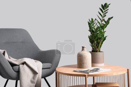 Photo for Wooden coffee table with houseplant and vase near cozy armchair on grey background - Royalty Free Image