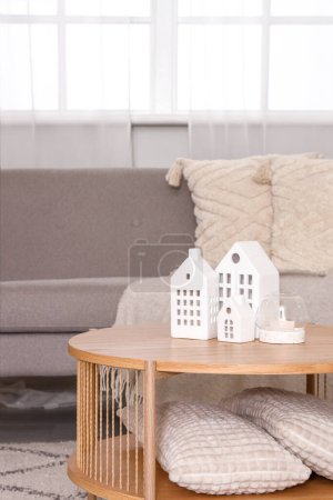 Coffee table with decorative houses and burning candle in interior of living room