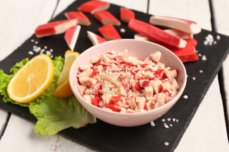Bowl with tasty chopped crab sticks on light wooden background