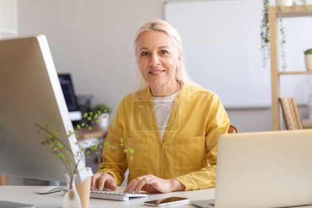 Photo for Mature female programmer working with computer at table in office - Royalty Free Image