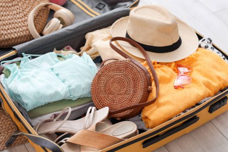 Open suitcase with beach accessories on floor in bedroom, closeup