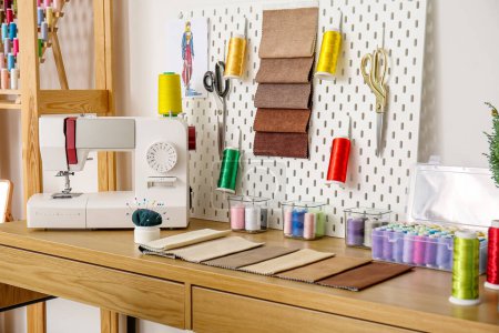 Tailor's workplace with sewing machine, thread spools and pegboard in atelier