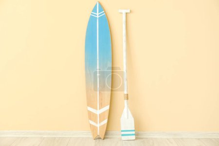 Foto de Tabla de surf de madera con paleta cerca de la pared beige - Imagen libre de derechos