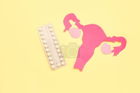 Téléchargez les photos : Utérus de papier avec des pilules hormonales sur fond jaune - en image libre de droit