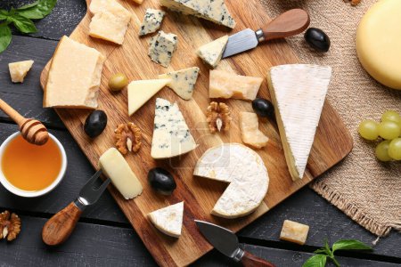 Foto de Tablero con diferentes tipos de sabroso queso y miel sobre fondo de madera oscura - Imagen libre de derechos