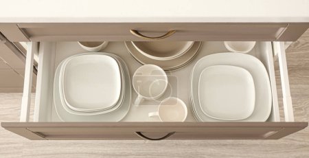 Open drawer with clean dishes and cups in kitchen, top view