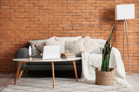 Foto de Interior de la sala de estar con sofá acogedor, ordenador portátil moderno en la mesa y cactus en olla - Imagen libre de derechos