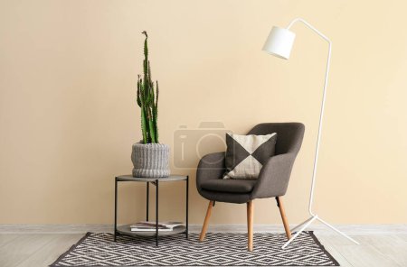 Foto de Acogedor sillón y gran cactus en maceta en la mesa cerca de la pared beige - Imagen libre de derechos