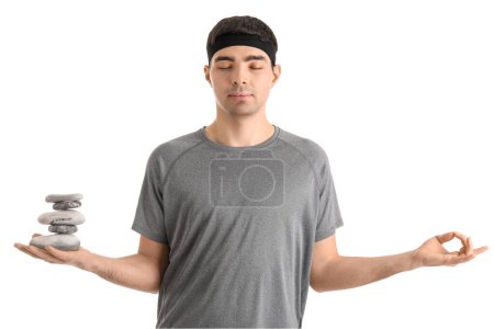 Sportlicher junger Mann mit Wellnesssteinen, die auf weißem Hintergrund meditieren. Gleichgewichtskonzept