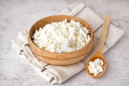 Photo for Bowl and spoon with tasty cottage cheese on light grunge background - Royalty Free Image