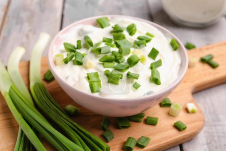 Photo for Bowl of tasty sour cream with green onion on light wooden background, closeup - Royalty Free Image