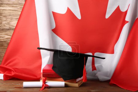 Graduation hat with diploma, books and flag of Canada on wooden table