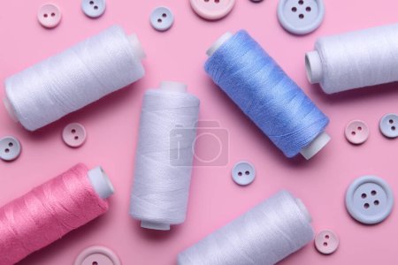 Composition with different thread spools and buttons on pink background, closeup