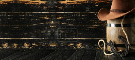 Cowboyhut mit Lauf, Hufeisen und Lasso auf dunklem Holzgrund mit Platz für Text