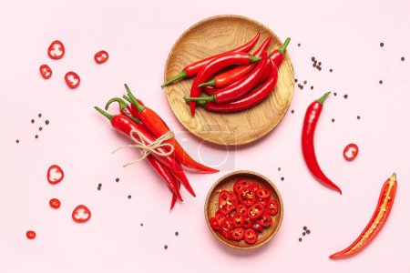 Tied fresh chili with plates of hot peppers on pink background