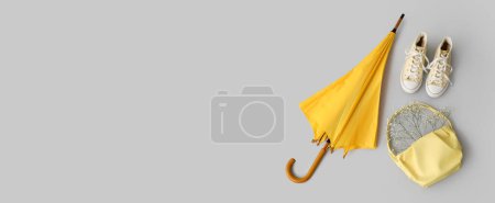 Yellow umbrella, gumshoes and female bag on grey background with space for text Poster 654450096