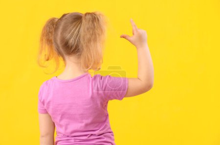 Photo for Funny little girl showing loser gesture on yellow background, back view - Royalty Free Image