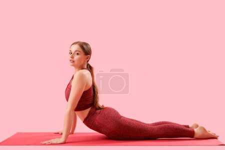 Sportliche junge Frau macht Yoga auf rosa Hintergrund