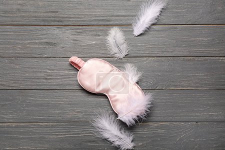 Photo for Sleeping masks and feathers on grey wooden background - Royalty Free Image