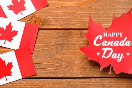 Rahmen aus Ahornblatt mit Text HAPPY CANADA DAY und Fahnen auf Holzgrund
