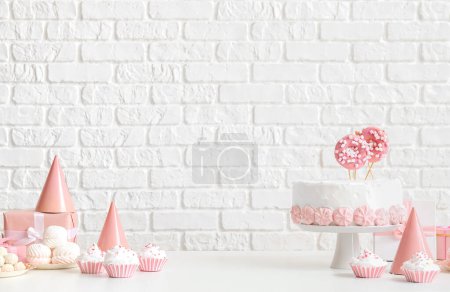 Photo for Birthday cake with sweets on white table near brick wall - Royalty Free Image