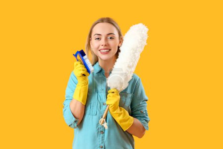 Young woman with cleaning brush and pp-duster on yellow background