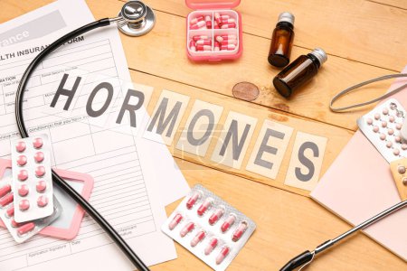 Word HORMONES with pills and medical supplies on wooden background