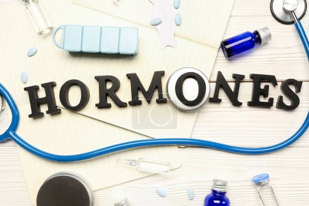 Foto de Word HORMONES con medicamentos, cuadernos y estetoscopio sobre fondo blanco de madera - Imagen libre de derechos
