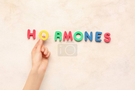Main féminine et mot HORMONES sur fond clair